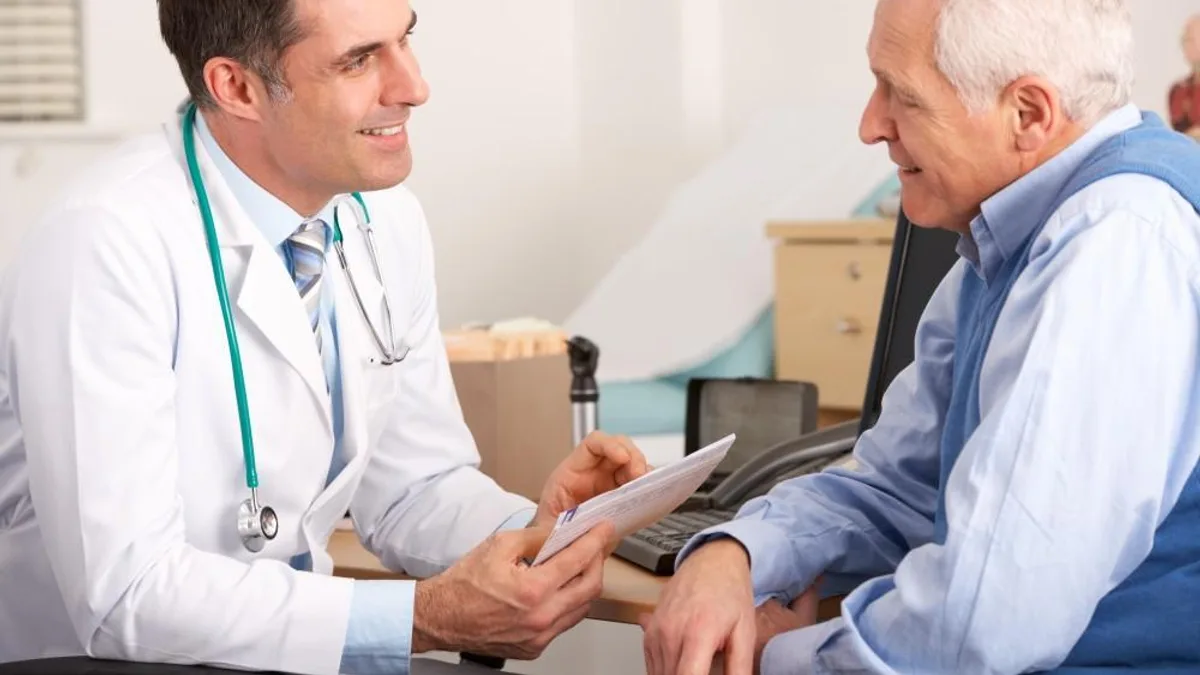A doctor with a stethoscope talking to an older patient and taking notes